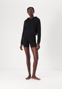 Svart kort zip-up hoodie med huva, med en slät textur och sidofickor, ihop med matchande svarta tajta shorts.