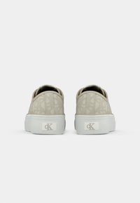 Un paio di sneakers beige con motivo e suole spesse bianche, viste da dietro, con il logo "cK" sui tasselli del tallone.