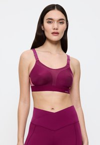 Viininpunainen urheiluliivit, joissa säädettävät olkaimet, muotoillut kupit ja verkkokuvioinnit sivuilla. Sileä pinta, jäsennelty muotoilu ja logo alaosassa.