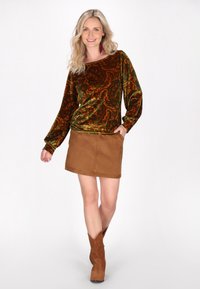 Samtgrünes und braunes Paisley-Oberteil mit langen Ärmeln, kombiniert mit einem beigen Wildleder-Minirock und braunen Wildleder-Stiefeletten mit spitzer Zehe.