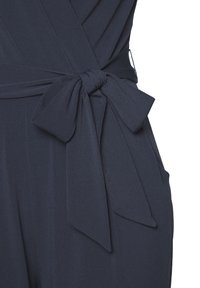 Mono azul marino con una textura suave, que presenta un detalle de cintura anudada y dos bolsillos laterales. La tela parece suave y ligera.