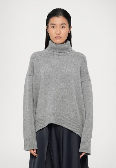 Grå, oversized strikket trøje med høj turtleneck, faldne skuldre og ribbet kant. Blød tekstur og en afslappet pasform.