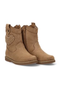 Botines de ante color beige con un detalle de corazón de peluche, cremallera lateral y suela cosida. Superficie texturada y diseño de puntera redonda.