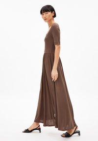 Brown maxi dress with short sleeves, fitted bodice, and flared skirt. Smooth, soft texture. Worn with black heeled sandals.