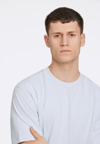 Vaaleansininen puuvillapaita, jossa on lyhyet hihat ja pyöreä kaula-aukko. Paidassa on sileä pinta ja rento, ylisuuri istuvuus.