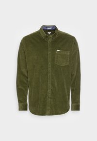 Olijfgroene corduroy blouse met lange mouwen, knoopsluiting, borstzak en geknoopte kraag op een effen achtergrond.