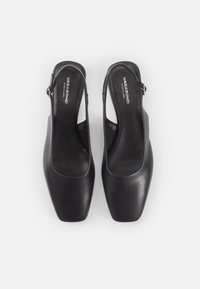 Des chaussures slingback en cuir noir avec un talon ouvert, un bout carré et un détail de boucle métallique. Semelle intérieure texturée et surface lisse.