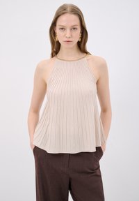 Beige geribbelde haltertop met een gouden kettinghalslijn, met een uitlopende zoom. Gepaard met bruine gestructureerde broek.