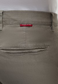 Pantaloni grigi con texture e tasca posteriore, caratterizzati da un'etichetta rossa "JOOP JEANS". Il tessuto presenta un motivo a pois fine e una forma sartoriale.