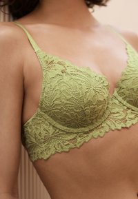 Hele rohelise lillemustriga pitsrinnahoidja, läbipaistva tekstuuriga, traaditoega ja reguleeritavate sangadega, kaunistatud laineliste äärtega.