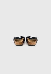 Sandales à enfiler en suede noir avec semelle en liège, semelle extérieure texturée et brides noires. Conçues pour le confort et une utilisation décontractée.