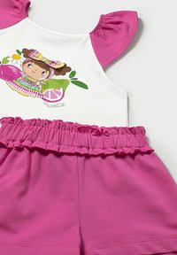 Top bianco senza maniche con maniche arricciate rosa, caratterizzato da un grafiche di un personaggio colorato. Pantaloni corti rosa con vita arricciata.