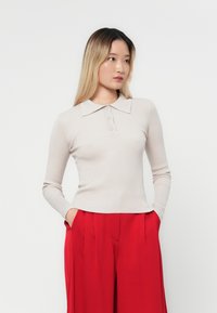 Beige ribbet langermet topp med krage, med tre knapper, paired med røde vide bukser. Glatt tekstur, tettsittende silhuett.
