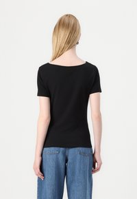 Svart kortärmad t-shirt med vid båtringning, tillverkad av bomull. Matchas med högmidjade, löst sittande blå denimjeans.