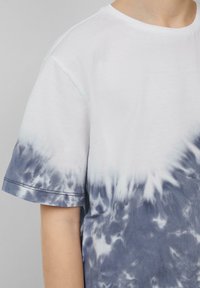 Katoenen t-shirt met een witte bovenkant die overgaat in een blauw tie-dye patroon aan de onderkant. Korte mouwen met een ronde hals en zichtbare stikseldetails.