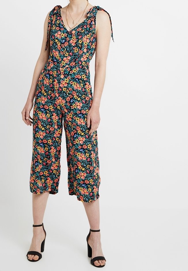 Combinaison florale avec un fond noir et des motifs roses, oranges et verts. Décolleté en V et jambes larges coupées. Bretelles ajustables à nouer.