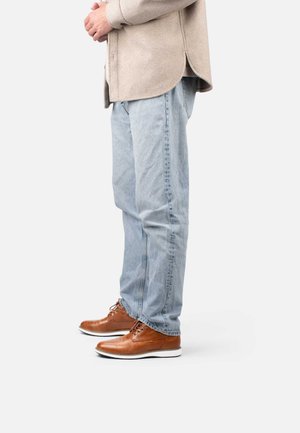 Tan leather shoes with white sole, light blue denim jeans, and a beige wool shirt with curved hem, shown in a side view.