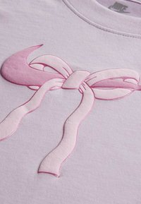 Felpa di un leggero viola con un proeminenze design a fiocco rosa, caratterizzato da texture lisce e lucide e dettagli di ombreggiatura delicati.