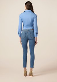 Blusa de color azul claro, con cuello y mangas largas con detalles en los puños, combinada con jeans oscuros ajustados y tacones beiges.