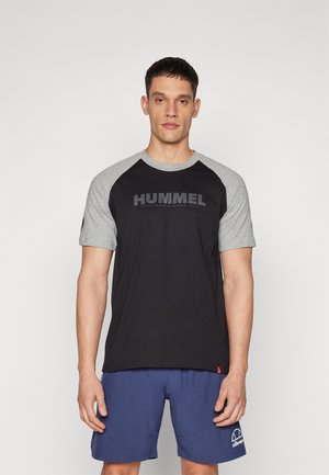 T-shirt à manches courtes avec un corps noir et des manches raglan grises, arborant un grand logo "HUMMEL" noir sur le devant. Texture de tissu douce.