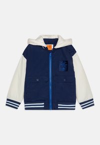 Veste bleu marine avec une capuche blanche, fermeture éclair, deux poches avant, poignets rayés et un logo sur patch. Fabriquée en tissu léger.
