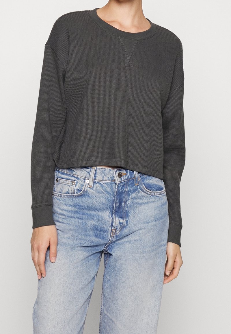 Sweatshirt corto a coste grigio scuro con maniche lunghe e scollatura rotonda, abbinato a jeans dritti leggeri e strappati di colore blu.