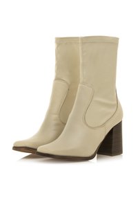 Botas de tobillo beige hechas de cuero liso con punta afilada y paneles laterales elásticos, que cuentan con un tacón de bloque texturizado.