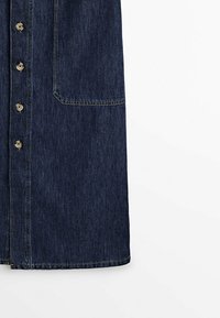 Jupe en denim bleu foncé avec boutons sur le devant et grande poche latérale, bord ourlé sur fond blanc.