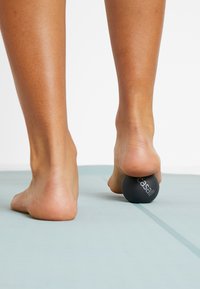 Black massage ball being pressed under a bare foot on a light blue mat, showcasing a smooth texture and round shape.