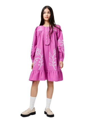 Rosa Baumwollkleid mit weißer Blumenstickerei, gerafftem Saum und geknöpfter Vorderseite. Lange Ärmel und legerer Schnitt. Gestylt mit beigefarbenen Loafers.