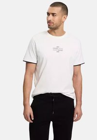 Biała koszulka z krótkim rękawem z czarnymi wykończeniami na rękawach; z nadrukiem w czarnym kolorze z nazwą marki. Połączona z czarnymi spodniami z troczkami.