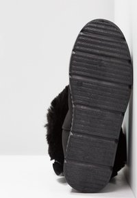 Svart känga med en texturerad gummisula och mjukt foder av päls. Sulan har horisontella spår för bättre grepp och hållbarhet.