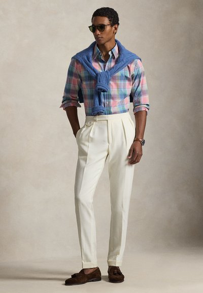 Light blue crew-neck sweater tied around the shoulders, multicolored plaid button-up shirt, white pleated trousers, brown loafers, sunglasses.
