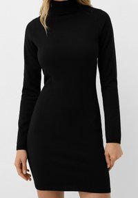 Robe noire à col roulé en tissu tricoté côtelé, avec des manches longues et une silhouette ajustée. Design simple sans motifs ni accents.