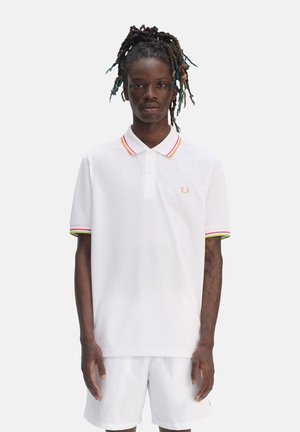 Camisa polo blanca con cuello de tres botones, que presenta rayas multicolores en rojo, rosa y verde en el cuello y los puños de las mangas. Logotipo dorado en el pecho.