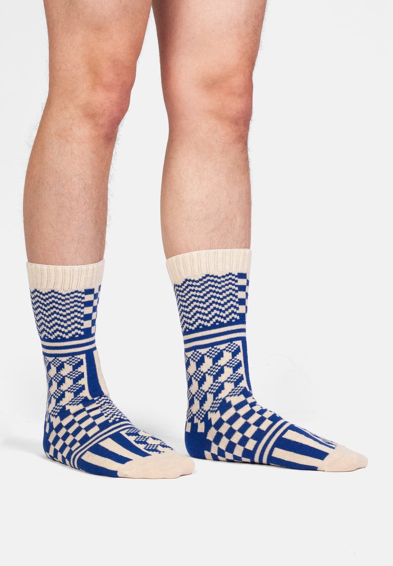 Calzini lavorati a maglia con motivi geometrici blu e crema, caratterizzati da un risvolto a coste e un mix di design a scacchi e onde.