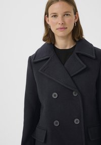 Tamsiai mėlynas vilnos peacoatas su dvigubu sagų užsegimu, plačia išpjauta apykakle ir šoninėmis kišenėmis, pasižymintis minkšta tekstūra ir pritaikytu siluetu.