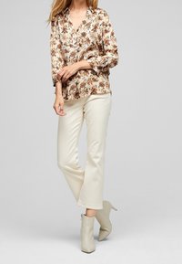 Blouse florale avec un design à col en V dans des tons crème et marron, associée à un pantalon crème et des bottines beige clair.