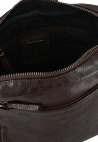 Bolso de cuero marrón con un acabado texturizado, cierre de cremallera y bolsillo interior, que cuenta con un forro de tela oscura y un discreto parche con logo.