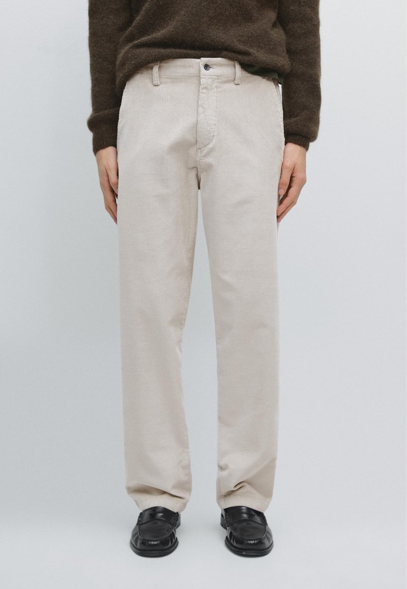 Beige corduroy pants with a straight leg design, featuring a button closure and front pockets, paired with black shoes.