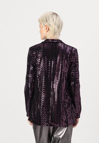 Blazer noir recouvert de sequins roses, avec un col classique et des manches longues, le tissu a une texture scintillante qui réfléchit la lumière.