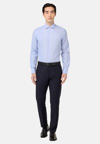 Svetlomodrá košeľa na gombíky s špicatým golierom, nosená s tmavomodrými nohavicami a čiernym opaskom. Topánky sú z čiernej kože.