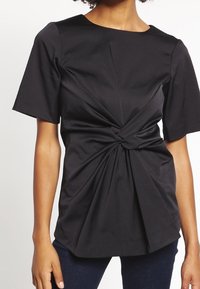 Černý krátký rukáv top s kulatým výstřihem, který má zkroucený přední design a strukturovanou látku pro dokonale padnoucí střih.