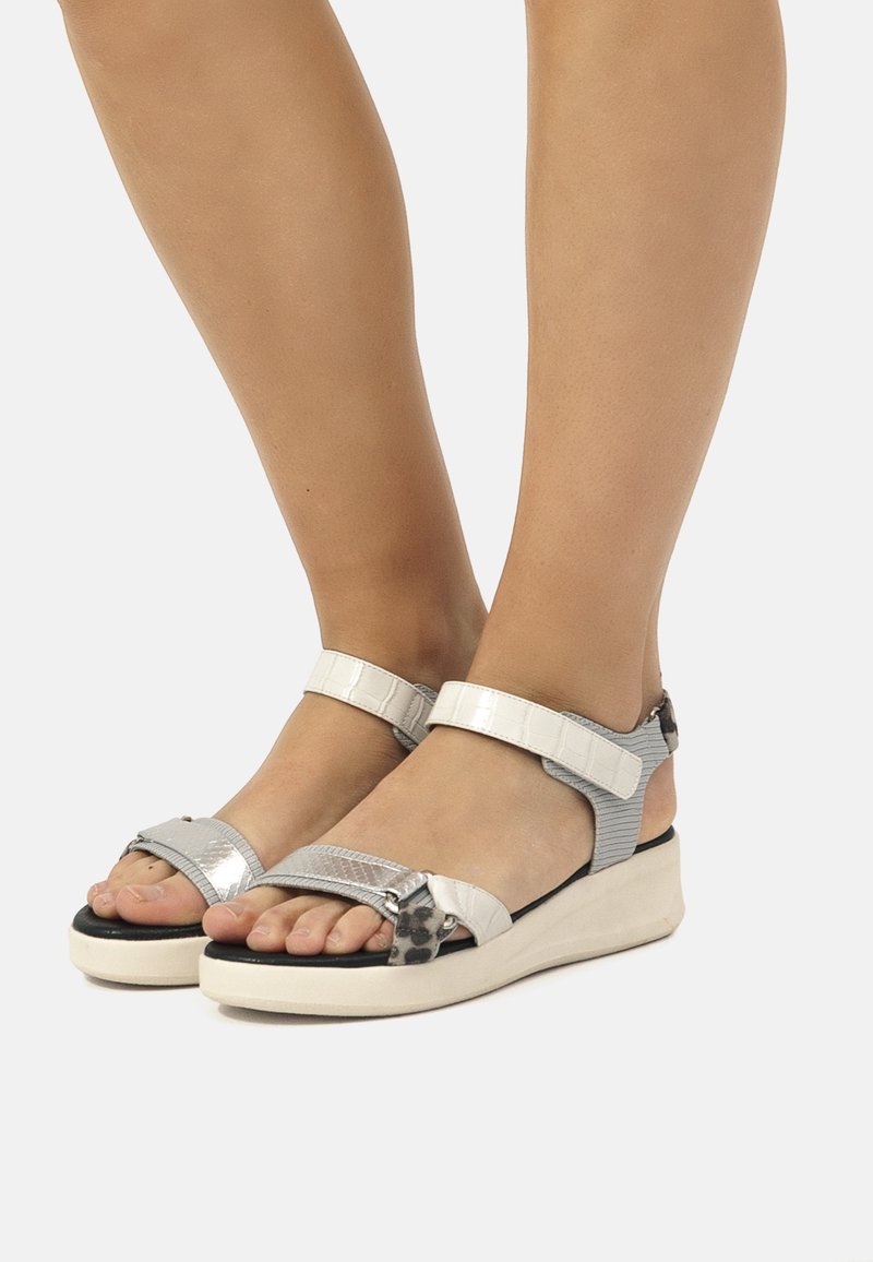 Sandalias plateadas y blancas con correas ajustables, material texturizado, suela plana y un pequeño tacón cuña; presenta un sutil detalle de estampado animal.