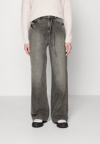 Pantalones de denim gris de pierna ancha con un acabado desgastado, que cuentan con una cintura con cordón, bolsillos laterales y un corte relajado. Combinados con calzado negro.