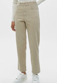 Beige corduroy broek met een hoge taille en rechte pasvorm, voorzien van zijzakken en een knoopsluiting, gecombineerd met witte sportschoenen.