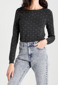 Szary sweter z długim rękawem w białe groszki, z okrągłym dekoltem, w połączeniu z jasnoniebieskimi, przetartymi jeansami z wysokim stanem.