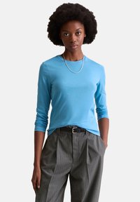 Light blue long-sleeve t-shirt in a soft cotton blend, paired with gray pinstriped trousers and a black belt, featuring a round neckline.