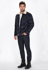 Sort og blå ternet flannel jakke med en kridhvid sherpa-krave, to brystlommer, parret med mørke jeans og sorte snørebåndsstøvler.