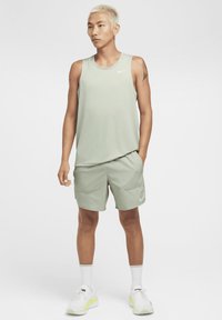 Roupa desportiva masculina verde-claro composta por uma camisola sem mangas e calções, feita de tecido que absorve a humidade, com um logótipo no peito e na lateral.